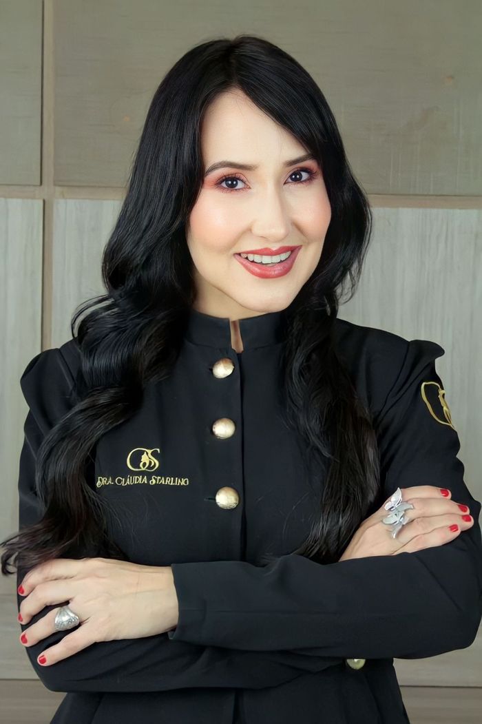 Dra. Cláudia Starling de jaleco preto com o logotipo da clínica, braços cruzados